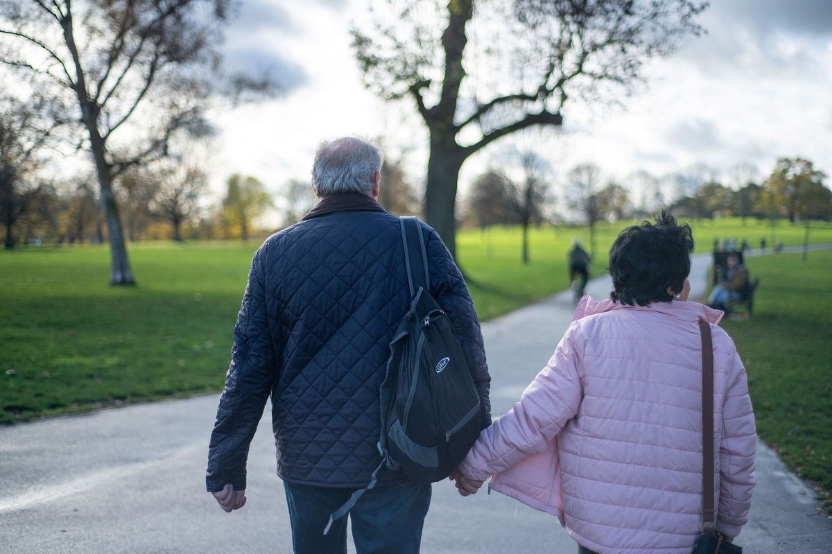 Man and woman walking away from camera in a park holding hands